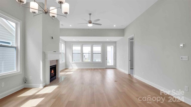 unfurnished living room with ceiling fan with notable chandelier and light hardwood / wood-style floors