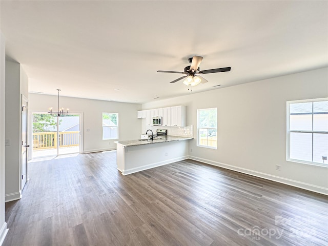 unfurnished living room featuring a healthy amount of sunlight, dark wood-type flooring, sink, and ceiling fan with notable chandelier