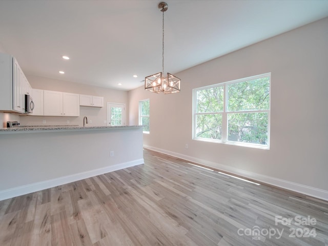 kitchen featuring white cabinets, light stone countertops, a chandelier, pendant lighting, and light hardwood / wood-style flooring