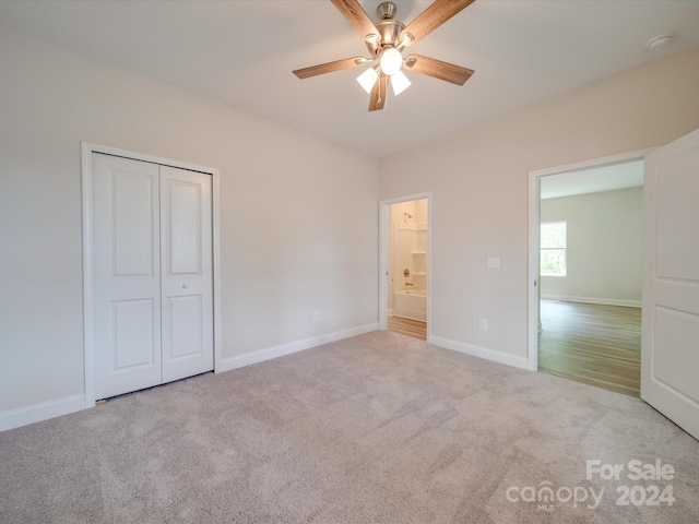 unfurnished bedroom featuring ceiling fan, light colored carpet, a closet, and ensuite bath