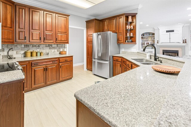 kitchen with decorative backsplash, sink, crown molding, stainless steel fridge, and light stone counters