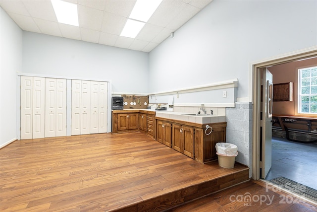 kitchen with a drop ceiling, tile countertops, light hardwood / wood-style flooring, and a towering ceiling