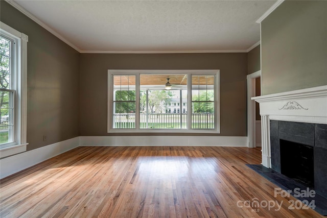 unfurnished living room featuring a textured ceiling, crown molding, light hardwood / wood-style floors, and a tiled fireplace