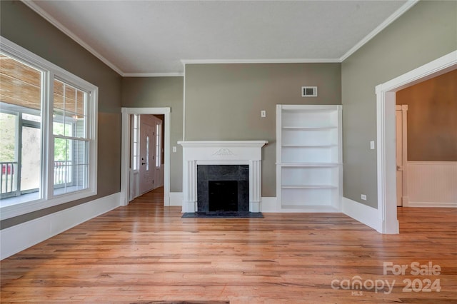 unfurnished living room with light hardwood / wood-style floors, a tile fireplace, built in features, and ornamental molding