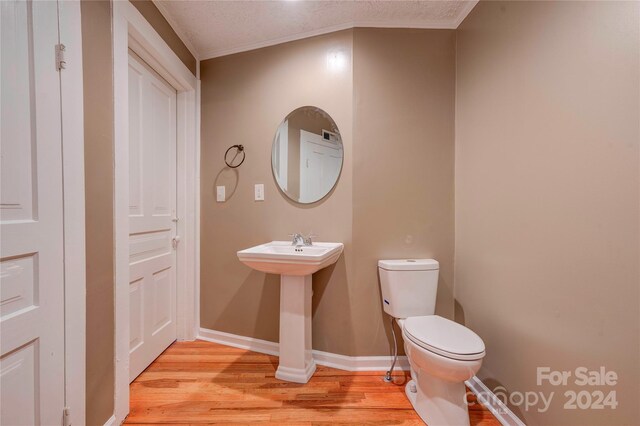 bathroom featuring a textured ceiling, toilet, crown molding, and hardwood / wood-style floors