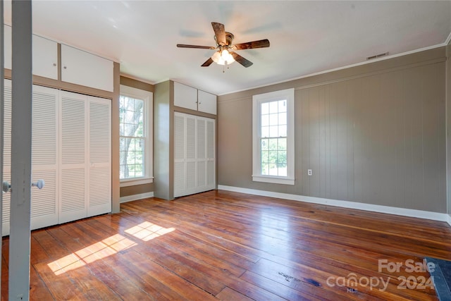 unfurnished bedroom featuring ceiling fan, two closets, wood-type flooring, and multiple windows