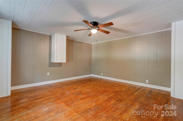 spare room with ceiling fan, wood-type flooring, and wood walls