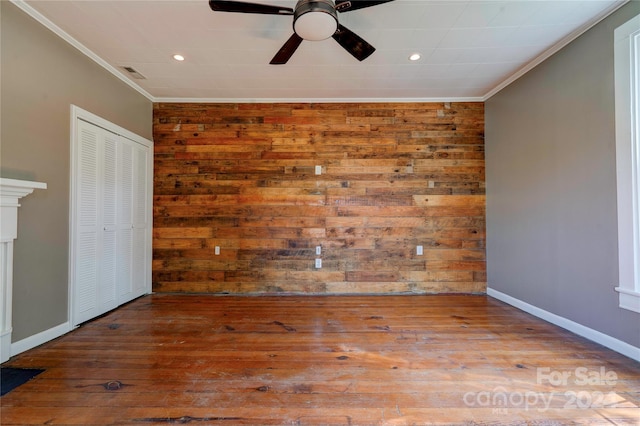 empty room with ceiling fan, ornamental molding, light hardwood / wood-style floors, and wooden walls