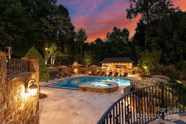 pool at dusk with a patio area and an in ground hot tub