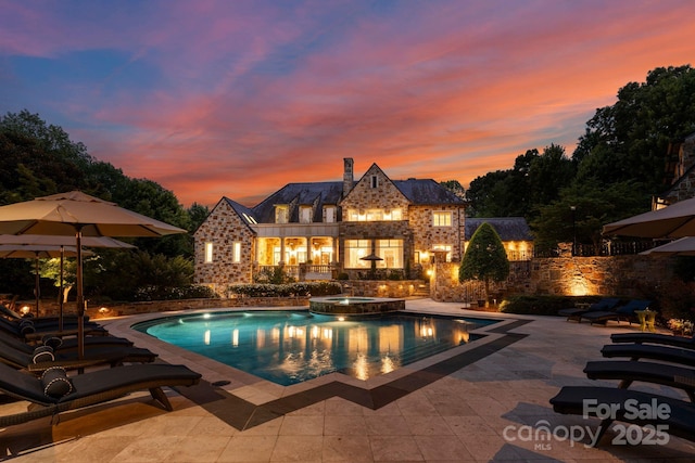 pool at dusk featuring an in ground hot tub and a patio