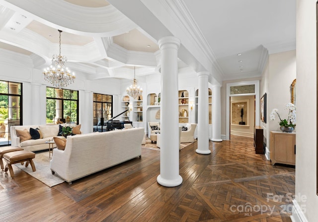 living room with coffered ceiling, crown molding, built in shelves, a notable chandelier, and decorative columns