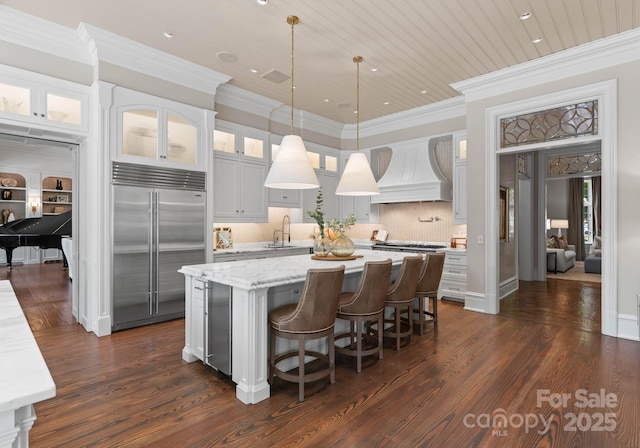 kitchen with premium range hood, a center island, white cabinetry, hanging light fixtures, and built in fridge