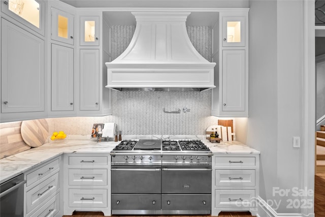 kitchen featuring appliances with stainless steel finishes, tasteful backsplash, light stone counters, custom range hood, and white cabinets