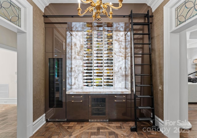 wine room featuring wine cooler, dark parquet floors, ornamental molding, and a notable chandelier