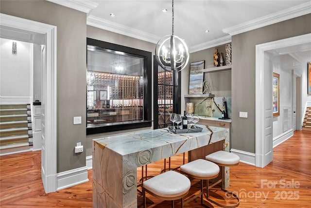 bar with light hardwood / wood-style floors, hanging light fixtures, a notable chandelier, and ornamental molding