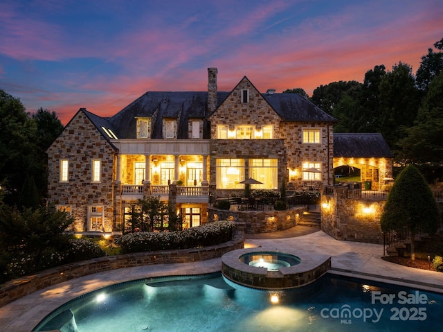 back house at dusk featuring a pool with hot tub