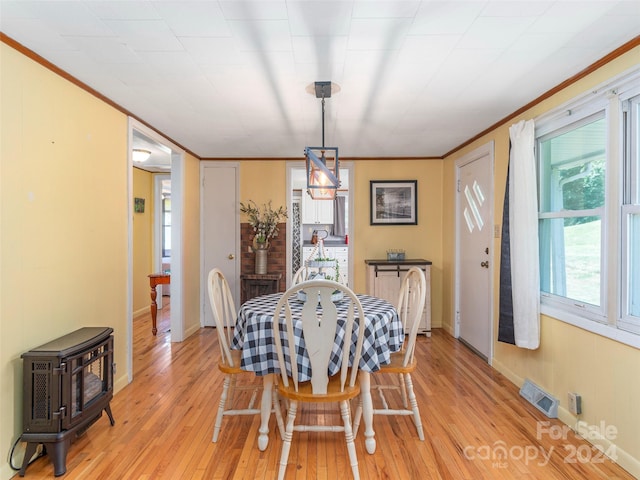 dining room featuring light hardwood / wood-style floors, a wood stove, and crown molding