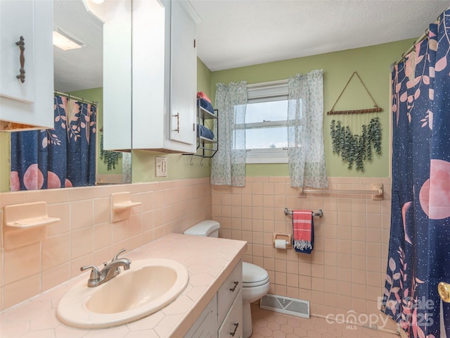 bathroom with toilet, a textured ceiling, tile walls, vanity, and tile patterned flooring