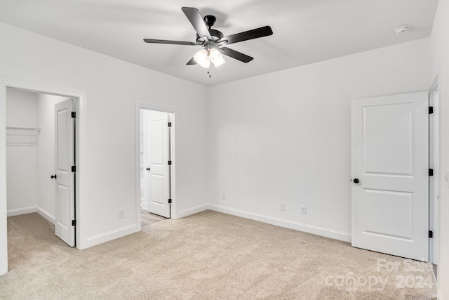 unfurnished bedroom featuring a spacious closet, light carpet, ceiling fan, and a closet