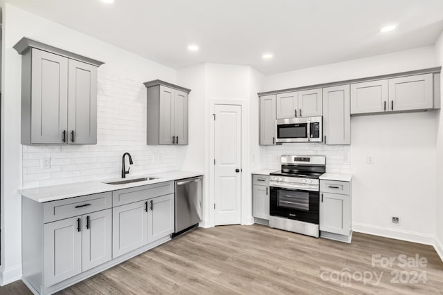 kitchen with tasteful backsplash, stainless steel appliances, light hardwood / wood-style floors, sink, and gray cabinetry