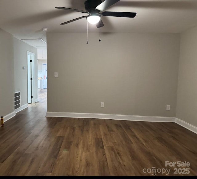 unfurnished room with a ceiling fan, visible vents, baseboards, dark wood-style floors, and attic access