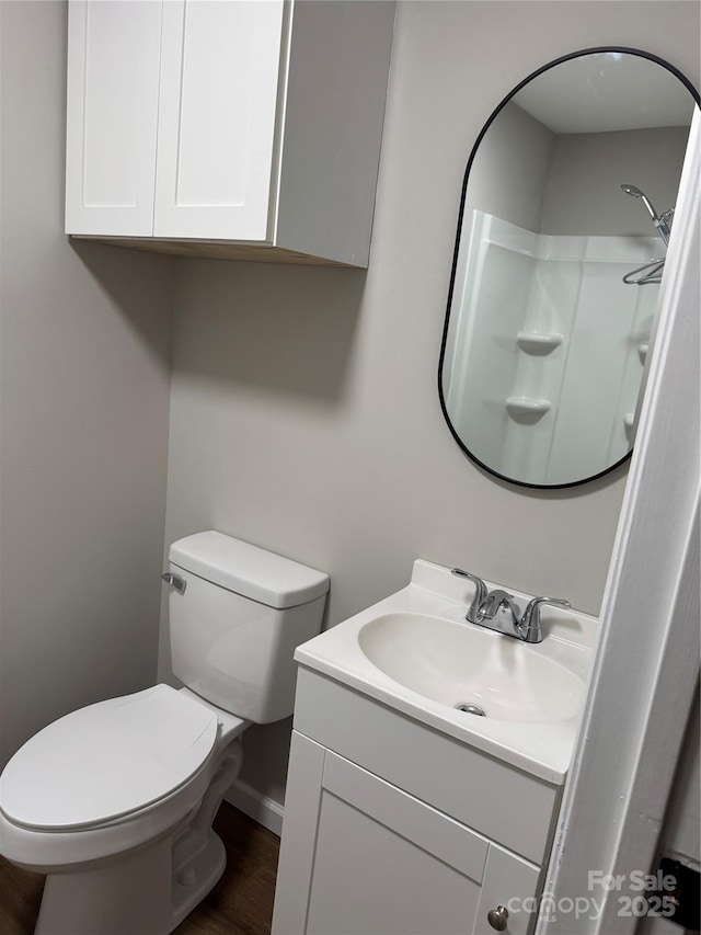 bathroom featuring toilet, wood finished floors, vanity, baseboards, and walk in shower