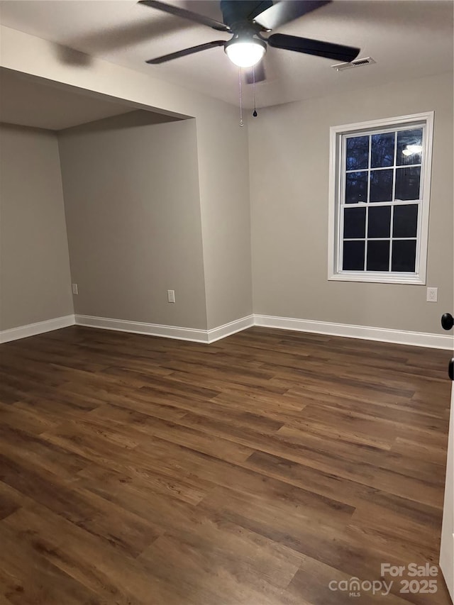 unfurnished room featuring a ceiling fan, visible vents, dark wood finished floors, and baseboards