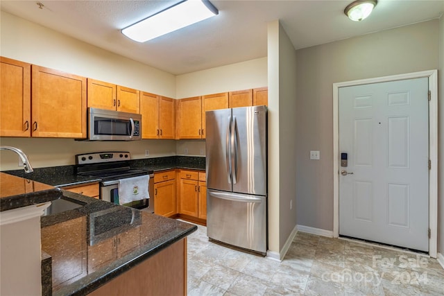 kitchen with appliances with stainless steel finishes, dark stone countertops, and kitchen peninsula