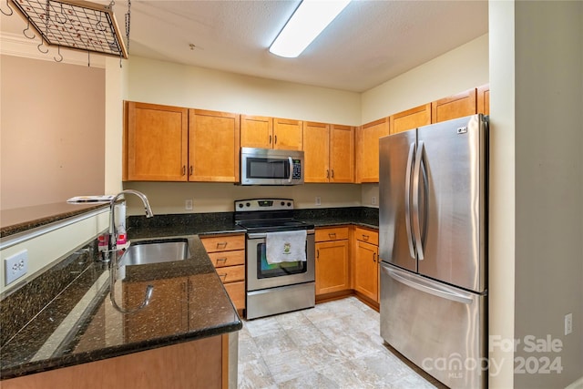 kitchen featuring dark stone countertops, kitchen peninsula, sink, stainless steel appliances, and a textured ceiling