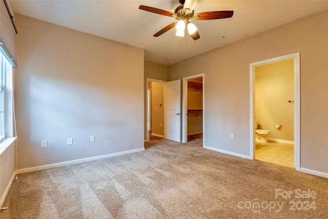 unfurnished bedroom featuring light carpet, ceiling fan, connected bathroom, a closet, and a walk in closet