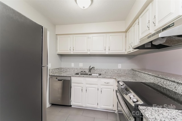 kitchen featuring white cabinets, light tile patterned floors, appliances with stainless steel finishes, light stone countertops, and sink