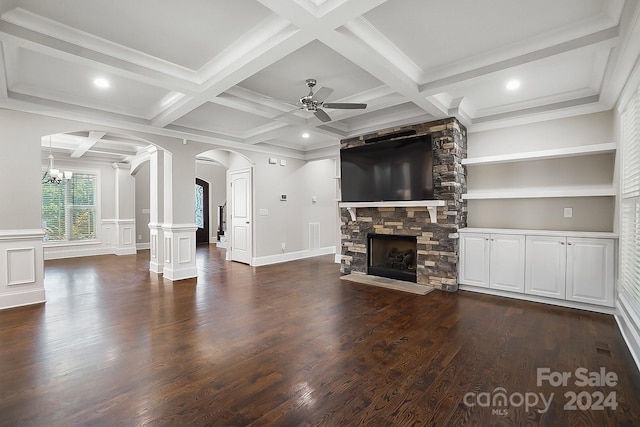 unfurnished living room with beamed ceiling, crown molding, coffered ceiling, a stone fireplace, and ceiling fan with notable chandelier