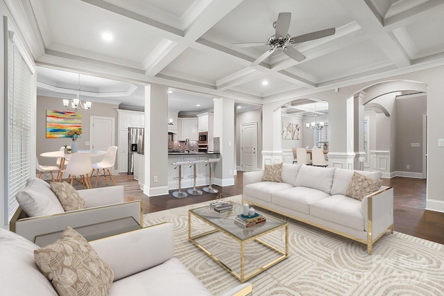 living room featuring coffered ceiling, dark wood-type flooring, crown molding, ceiling fan with notable chandelier, and beamed ceiling