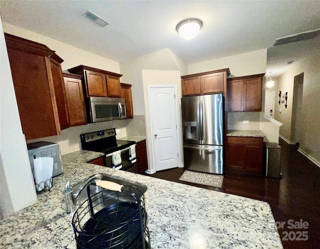 kitchen with stainless steel appliances, light stone counters, and visible vents