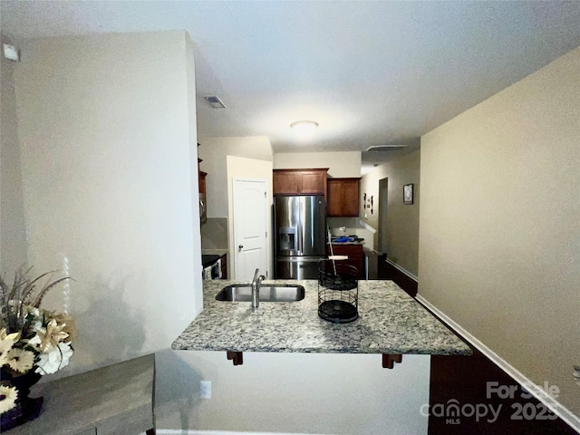 kitchen featuring a peninsula, a sink, light stone countertops, stainless steel fridge, and a kitchen bar