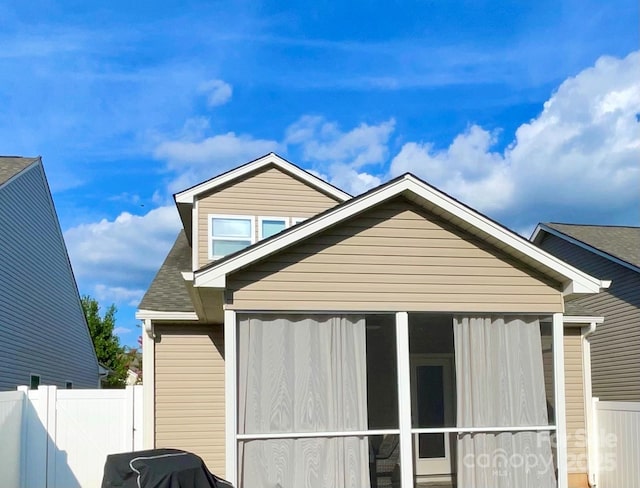 view of property exterior with a shingled roof, a sunroom, and fence