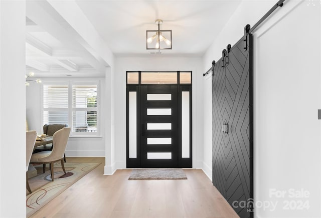 foyer entrance featuring wood-type flooring, a barn door, coffered ceiling, beam ceiling, and a notable chandelier