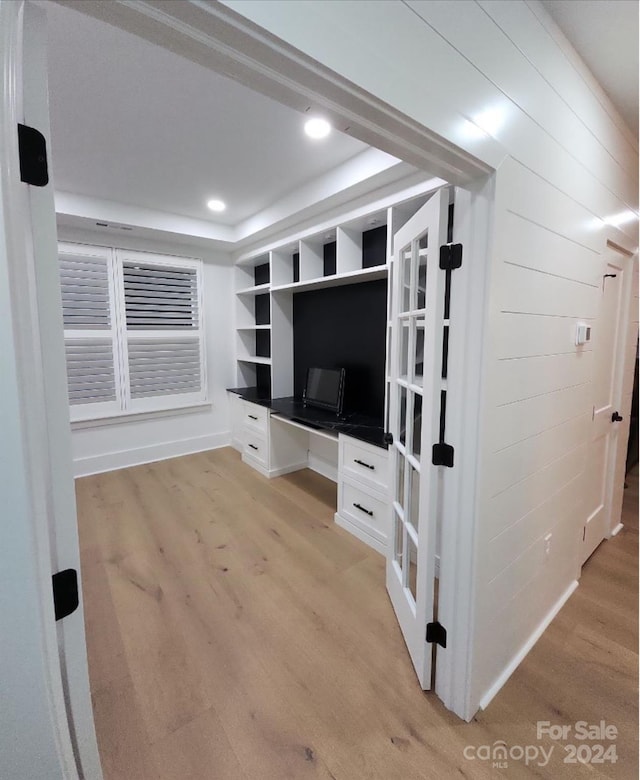 unfurnished living room featuring light hardwood / wood-style floors, built in desk, and a raised ceiling