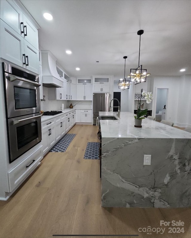 kitchen featuring stainless steel appliances, an inviting chandelier, light wood-type flooring, custom exhaust hood, and white cabinets