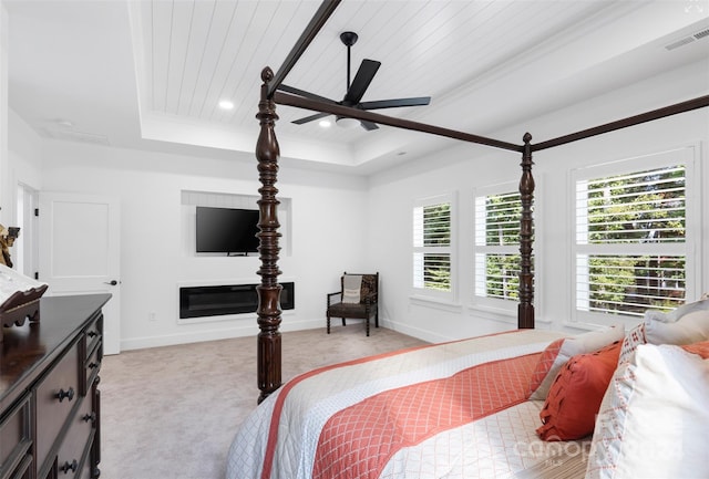 bedroom with multiple windows, light colored carpet, a tray ceiling, and ceiling fan