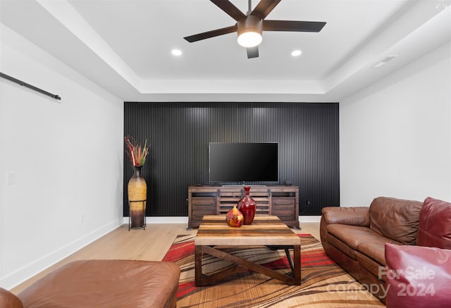 living room featuring ceiling fan, a raised ceiling, and light hardwood / wood-style flooring