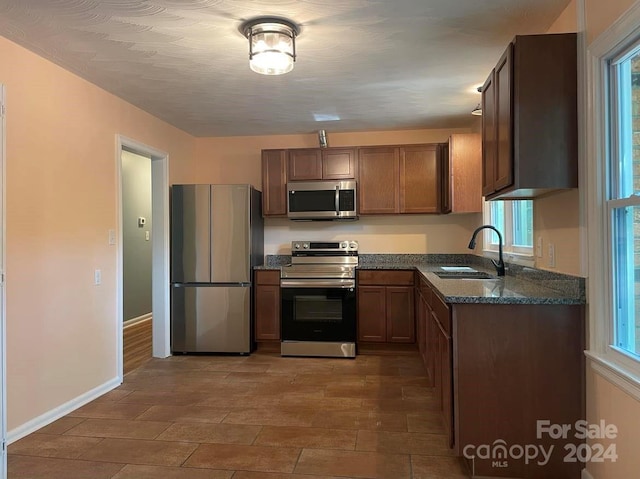 kitchen featuring a wealth of natural light, sink, appliances with stainless steel finishes, and dark stone counters