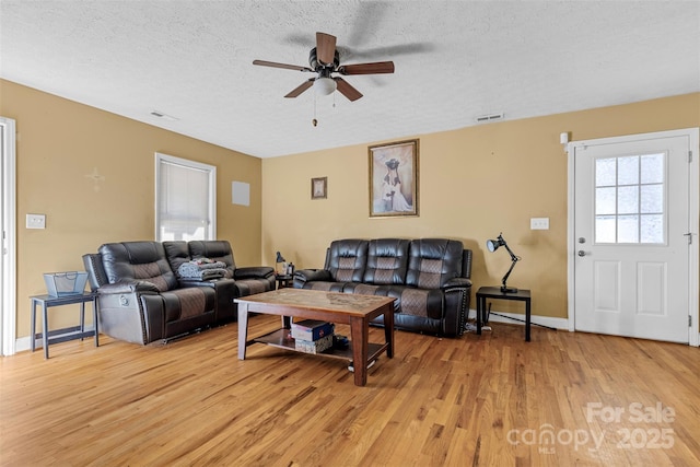 living room with ceiling fan, light wood-type flooring, and a textured ceiling