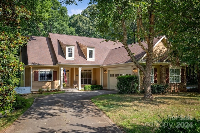 new england style home featuring covered porch, a garage, and a front yard