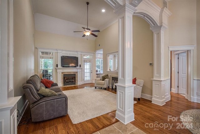 living room with ornate columns, ceiling fan, crown molding, a high ceiling, and a tiled fireplace