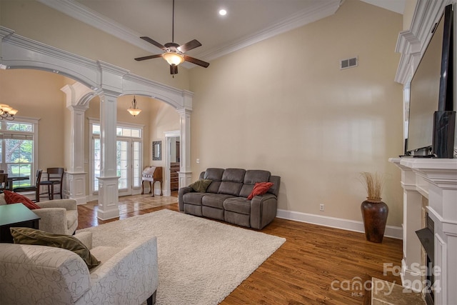 living room featuring crown molding, hardwood / wood-style flooring, ceiling fan, ornate columns, and a towering ceiling