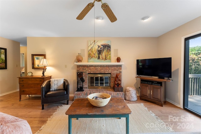 living room with ceiling fan, light wood-type flooring, and a brick fireplace