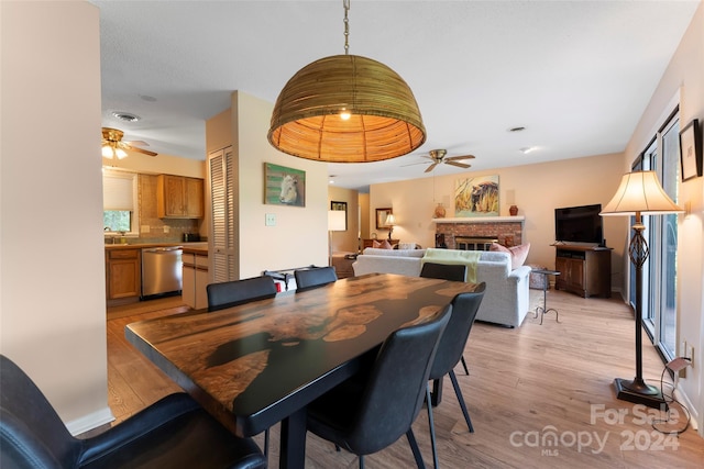 dining room with light hardwood / wood-style floors, a brick fireplace, and ceiling fan