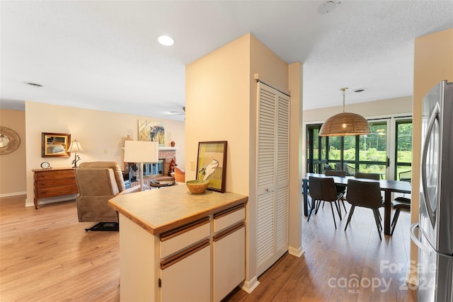 kitchen featuring decorative light fixtures, light wood-type flooring, stainless steel refrigerator, and a brick fireplace