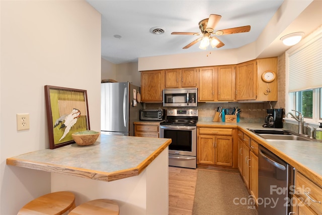 kitchen featuring kitchen peninsula, appliances with stainless steel finishes, backsplash, a kitchen breakfast bar, and sink